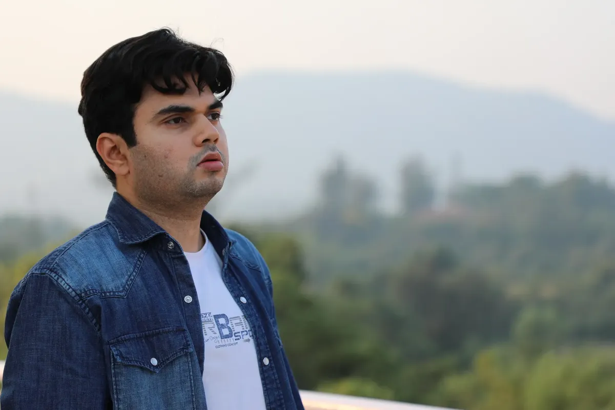 Young man wearing a denim jacket gazing outdoors with a blurred natural landscape behind.