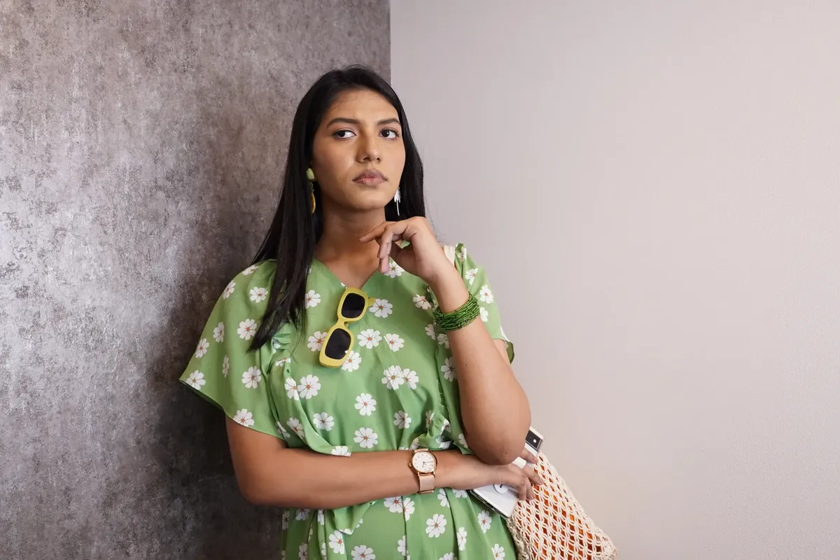Stylish woman in a green floral dress pondering indoors, exuding fashion and elegance.