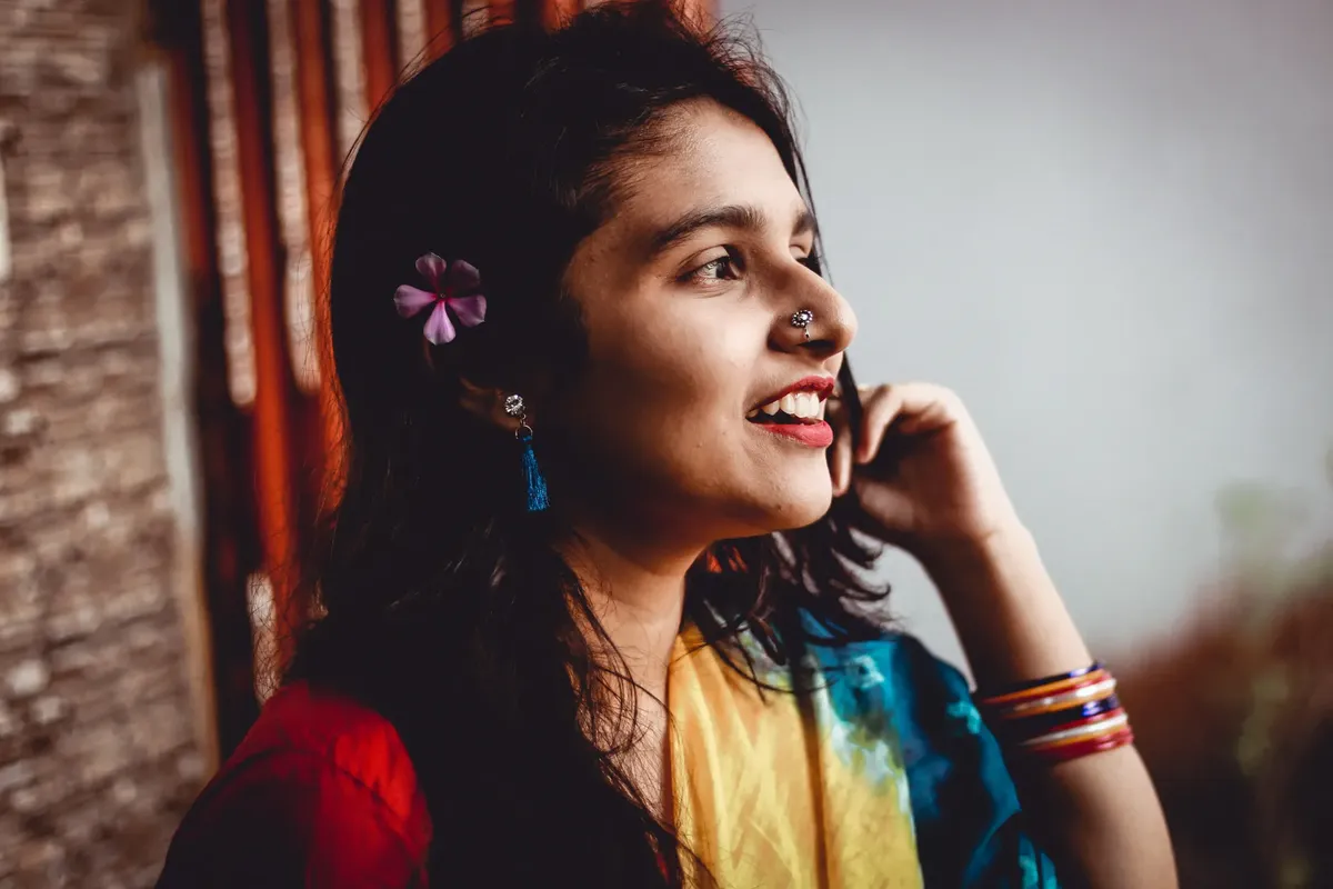 Side view of cheerful smiling Indian female with bright earrings and piercing in colorful sari on blurred background of terrace