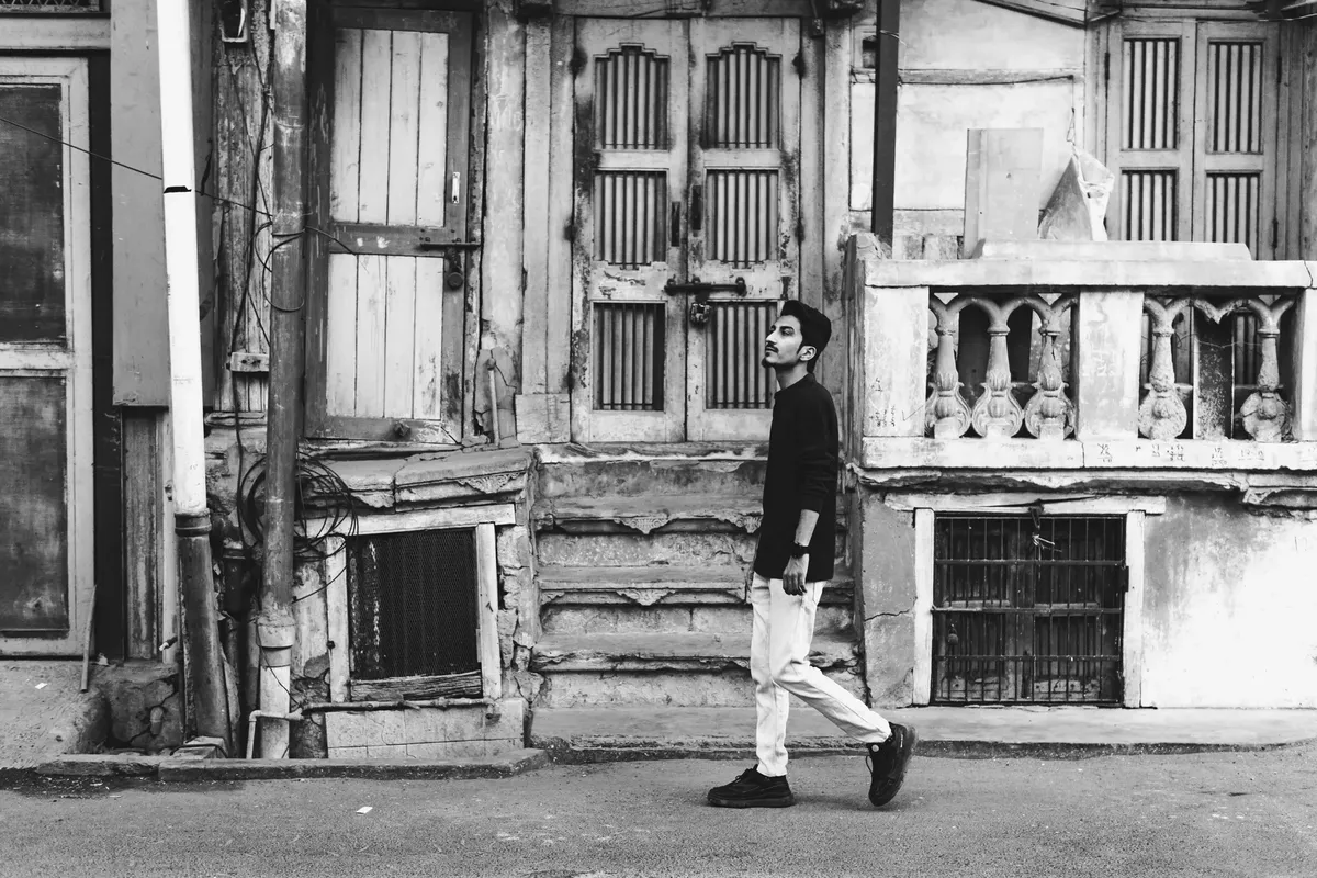 Black and white photo of a man walking past historic buildings in Ahmedabad, India.